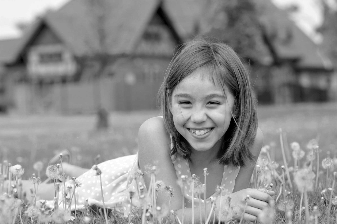 Black-and-white portrait of a smiling child lying in grass